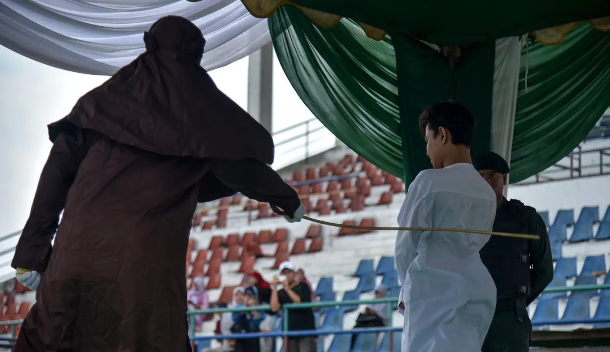 Seorang pria dicambuk setelah ketahuan melakukan hubungan seks pranikah di sebuah stadion di Lhokseumawe di provinsi Aceh (31/7/2019). Dua pria dan seorang wanita dicambuk secara terbuka sebanyak 100 kali karena melanggar hukum Islam di daerah tersebut. (AFP Photo/Rahmad Mirza)