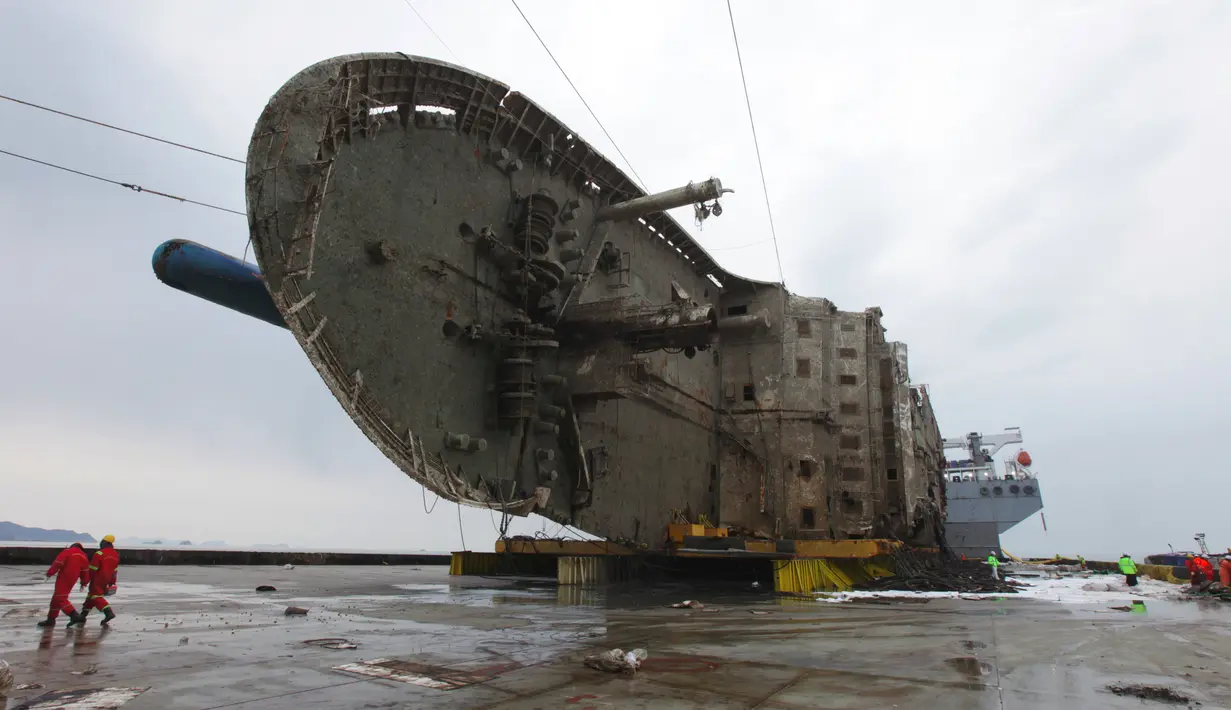 Petugas melintas didepan bangkai kapal Sewol yang berhasil diangkat di pulau barat daya Jindo, Korea Selatan (26/3). Kapal ini sebelumnya tenggelam hampir tiga tahun di kedalaman 44 meter. (HANDOUT / SOUTH KOREAN MARITIME MINISTRY / AFP)