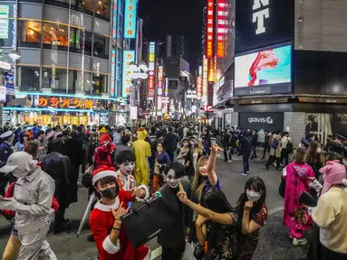 Para pejalan kaki dengan kostum berpose untuk foto ketika ribuan orang berkumpul di distrik Shibuya, area pertemuan populer untuk Halloween, di Tokyo, Minggu (31/10/2021). Daerah di sekitar Stasiun Shibuya dipadati anak-anak muda yang berdandan selama Halloween setiap tahun. (AP Photo/Kiichiro Sato)