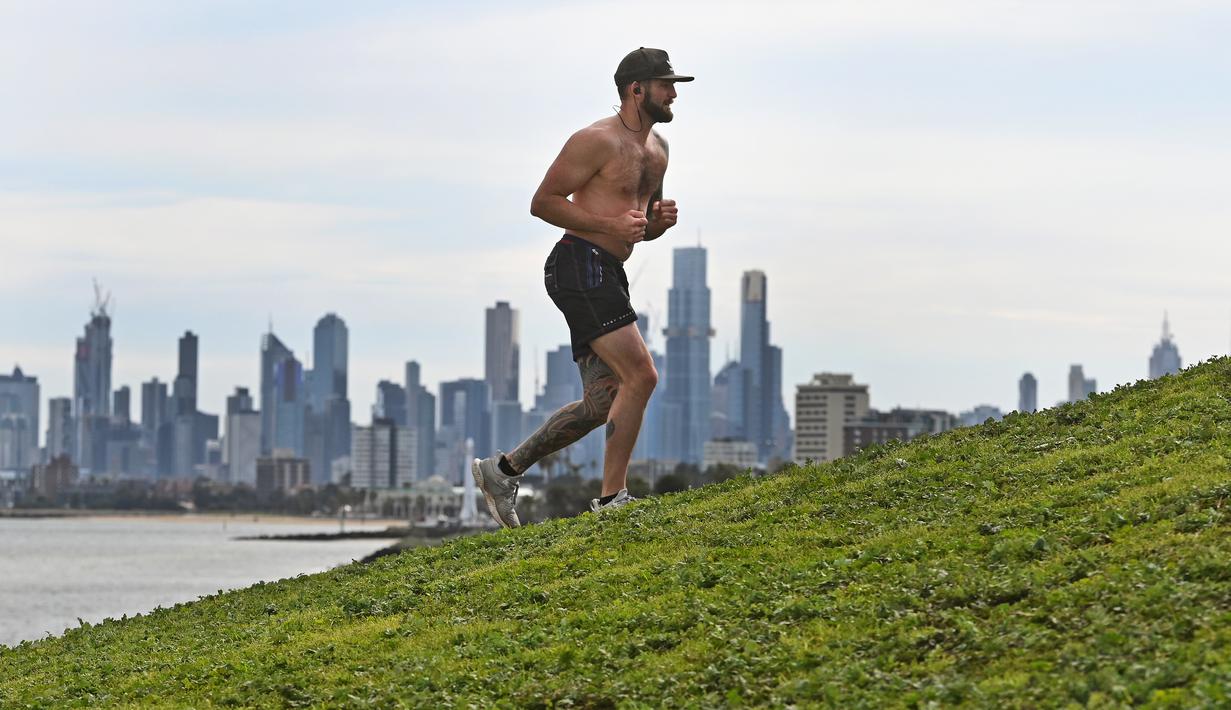 Seorang pria berlatih dengan latar belakang cakrawala Melbourne (11/8/2020). Negara bagian Victoria melaporkan 19 kematian akibat virus corona pada 11 Agustus, menjadikannya hari paling mematikan di negara itu dari pandemi meskipun jumlah kasus baru turun. (AFP/William West)