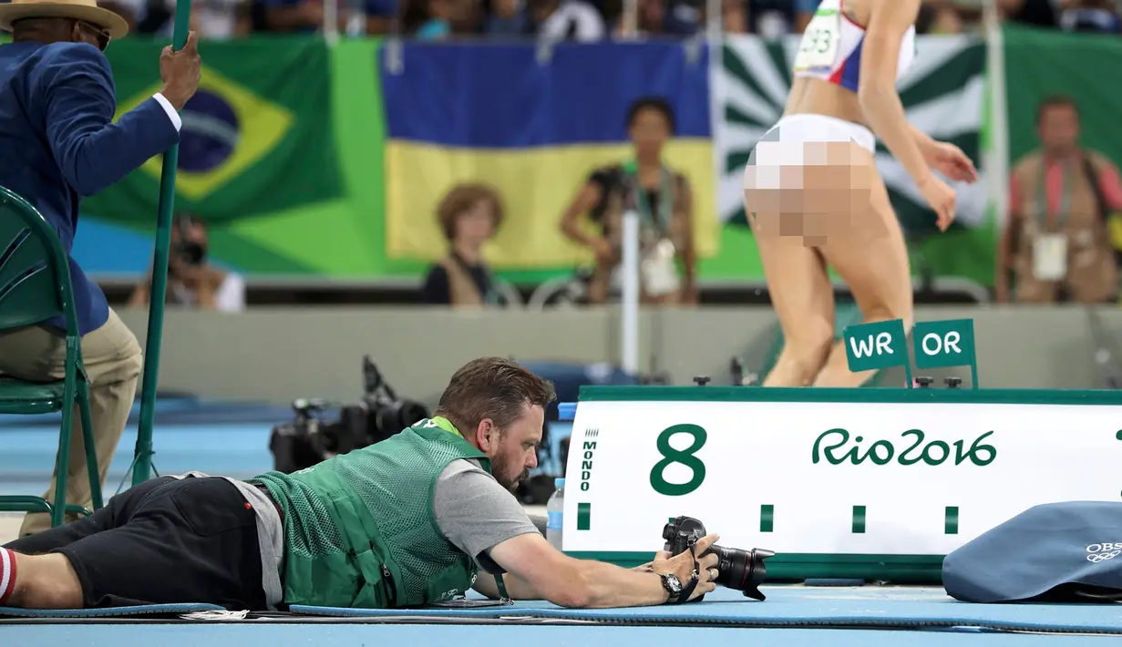 Seorang fotografer terlihat mengatur kameranya sambil tengkurap saat babak final lompat jauh putri pada Olimpiader Rio 2016, Rio de Janeiro, Brasil, (15/8). (REUTERS/Phil Noble)