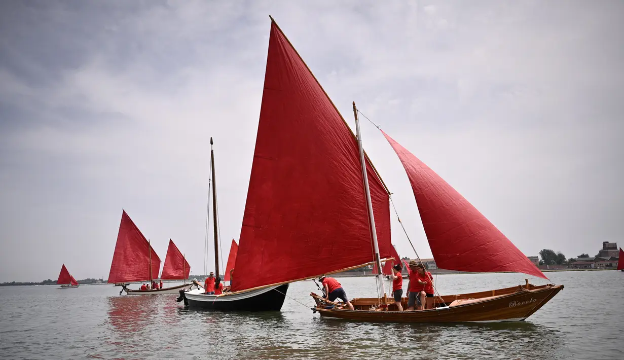 Anggota asosiasi pelayaran budaya berlayar dalam acara Regatta Merah di Venesia, Italia, Minggu (20/6/2021). Regatta Merah diselenggarakan oleh seniman AS Melissa Mc Gill. (MARCO BERTORELLO/AFP)