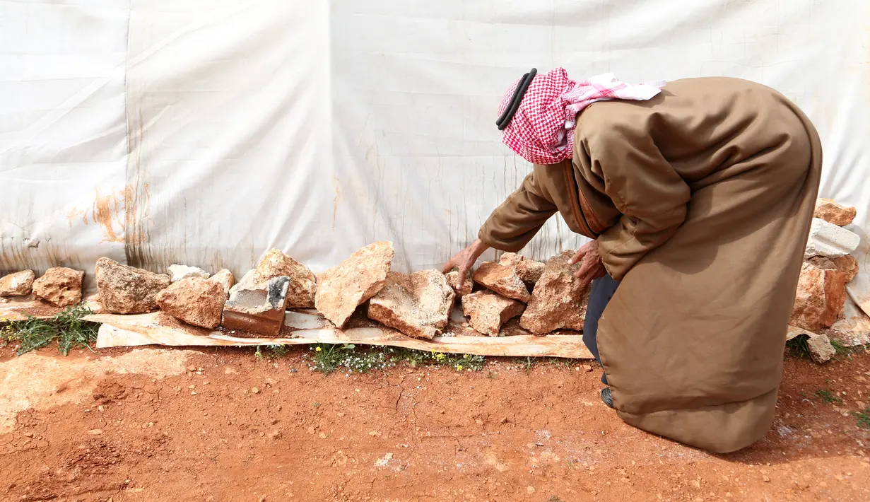 Abderrazaq Khatoun (83) menempatkan batu untuk melindungi salah satu tendanya dari angin di desa Harbanoush, di Idlib, Suriah pada 11 Maret 2021. Perang Suriah yang merampas 13 anak Khatoun dan salah satu istrinya, membuat kakek itu membesarkan 11 cucu yatim piatu sendirian. (Ahmad al-ATRASH/AFP)