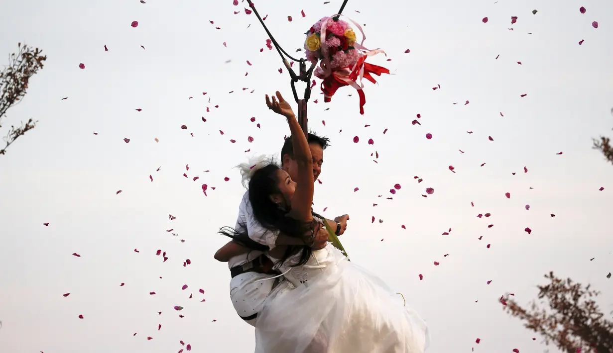 Sepasang pengantin membuang buket bunga sambil bergelantungan pada tali saat upacara pernikahan di Ratchaburi, Thailand, Sabtu (13/2). Upacara pernikahan tersebut diikuti empat pasang pengantin untuk menyambut Hari Valentine. (REUTERS/Athit Perawongmetha)