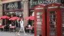 Sepasang kekasih berjalan melewati sebuah restoran di pusat kota London pada Kamis (3/6/2021). Pemerintah Inggris belum bisa memastikan akan sepenuhnya mencabut lockdown yang berakhir pada 21 Juni nanti meski kasus Covid-19 mengalami tren penurunan. (Tolga Akmen/AFP)