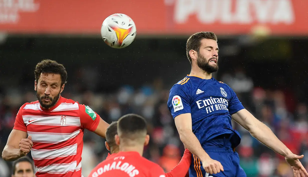 Bek Real Madrid Nacho Fernandez (kanan) menyundul bola dalam laga lanjutan Liga Spanyol melawan Granada di Stadion Nuevo Los Carmenes, Senin (22/11/2021) dini hari WIB.  Real Madrid menang telak dengan skor 4-1 atas tuan rumah Granada. (JORGE GUERRERO / AFP)
