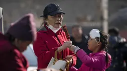Seorang anak mengenakan masker di dahinya berbagi haw Cina berlapis gula dengan kerabatnya di luar Menara Drum di Beijing, Senin (30/1/2023). Orang-orang China menikmati Tahun Baru Imlek dan mengunjungi berbagai lokasi wisata di kota-kota di sekitar China setelah pencabutan pembatasan COVID-19 yang kejam bulan lalu, memungkinkan banyak aspek kehidupan normal kembali. (AP Photo/Andy Wong)