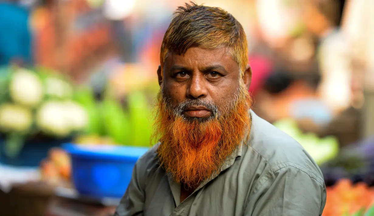 Dalam gambar yang diambil pada 24 Desember 2018, penjual sayur bernama Munir Hossain berpose dengan janggut oranye di Dhaka. Ternyata bukan hanya janggut saja yang mereka warnai, bagian rambut di kepala juga diwarnai dengan henna dan karena banyak yang menggunakannya. (MUNIR UZ ZAMAN / AFP)