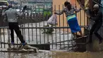 Pejalan kaki berjalan di pagar untuk menyebrang menyusuri jalan yang banjir menuju tempat kerja setelah hujan deras di Nairobi, Kenya (15/3). (AFP Photo/Simon Maina)