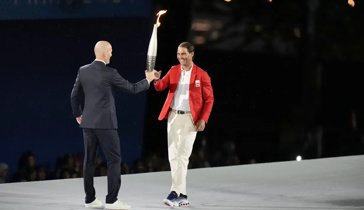 Petenis asal Spanyol, Rafael Nadal, menerima obor dari legenda Prancis, Zinedine Zidane, dalam acara pembukaan Olimpiade Paris 2024 di Sungai Seine, Prancis. (AP Photo/Natacha Pisarenko)