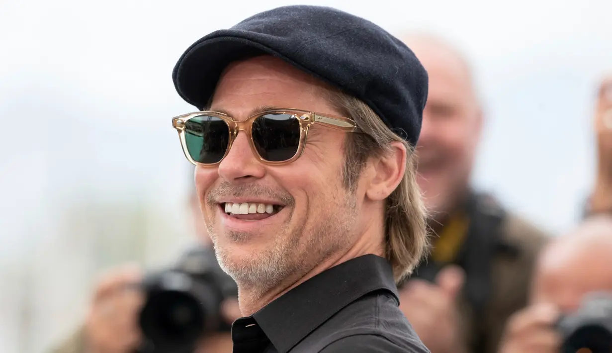 Aktor Brad Pitt tersenyum saat tiba menghadiri pemutaran film 'Once Upon a Time in Hollywood' selama Festival Film Cannes Internasional ke-72 di Prancis (22/5/2019).  Brad Pitt tampil santai mengenakan jeans hitam, kemeja polo hitam, kaca mata dan topi. (AP Photo/Joel C Ryan)