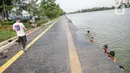 Seorang pria melihat anak-anak berenang di Danau Sunter, Jakarta, Selasa (2/2/2021). Minimnya lahan bermain anak membuat mereka memanfaatkan tempat yang tidak semestinya untuk bermain karena adanya risiko hanyut dan tenggelam bila tidak mampu untuk berenang. (Liputan6.com/Faizal Fanani)