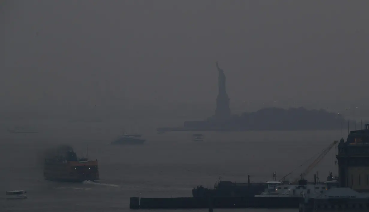 Feri Staten Island berangkat dari terminal Manhattan melalui kabut asap dengan Patung Liberty nyaris tidak terlihat, di New York, Selasa (20/7/2021). Lebih dari 60 kebakaran hutan melanda sekitar 10 negara bagian di AS, menyebabkan langit berkabut hingga New York.  (AP Photo/Julie Jacobson)