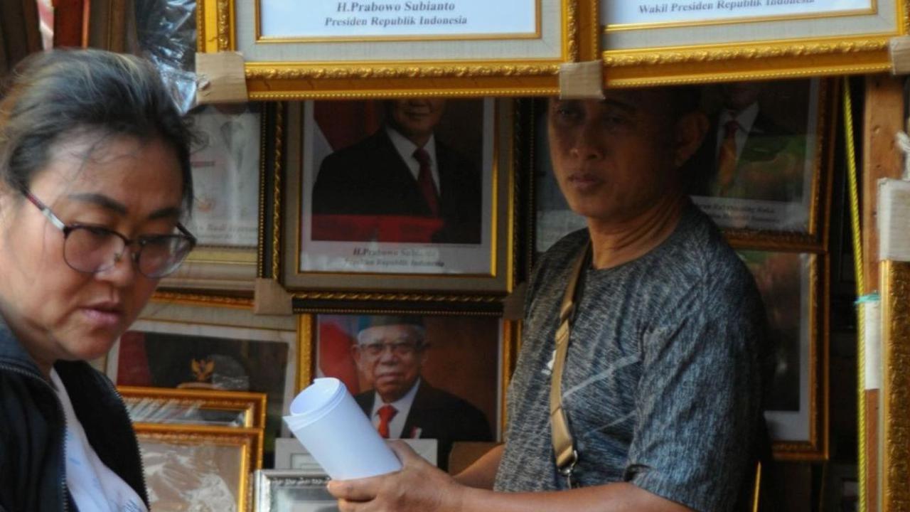 Pedagang bingkai foto saat melayani pembeli yang memesan gambar tersebut di Pasar Baru Jakarta, Senin (22/4/2024). Foto: merdeka.com / Imam Buhori