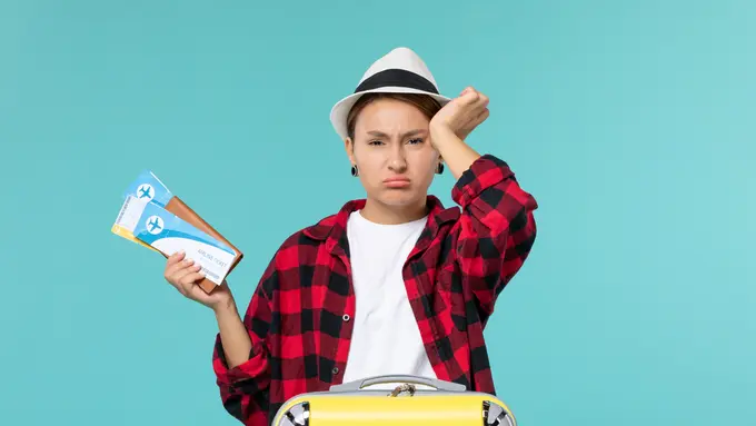 Seorang perempuan dengan topi dan sebuah koper tampak cemberut sambil memegang dahinya (Foto Dok: Freepik/KamranAydinov)