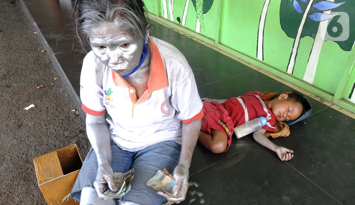 Seorang ibu menghitung uang hasil mengamennya sebagai "Manusia Silver " di salah satu sudut toko di kawasan perempatan Gaplek, Pamulang, Tangerang Selatan, Sabtu (16/1/2021). Ibu tersebut bersama anaknya mendapat penghasilan sekitar 50 ribu per hari sebagai Manusia Silver (merdeka.com/Arie Basuki)