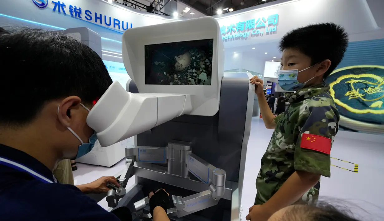 Seorang anak menonton saat seorang pekerja mengoperasikan robot bedah dari jarak jauh yang menunjukkan ketangkasannya dengan mengeluarkan cangkang dari telur saat Konferensi Robot Dunia di Yichuang International Conference and Exhibition Centre, Beijing, China, 19 Agustus 2022. (AP Photo/Ng Han Guan)