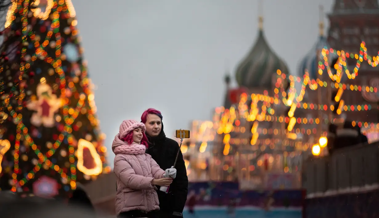 Sepasang kekasih berswafoto dengan latar belakang pohon Natal dekat Gereja Katedral St. Basil di Lapangan Merah, Moskow, Rusia, Selasa (4/12). (AP Photo/Alexander Zemlianichenko)