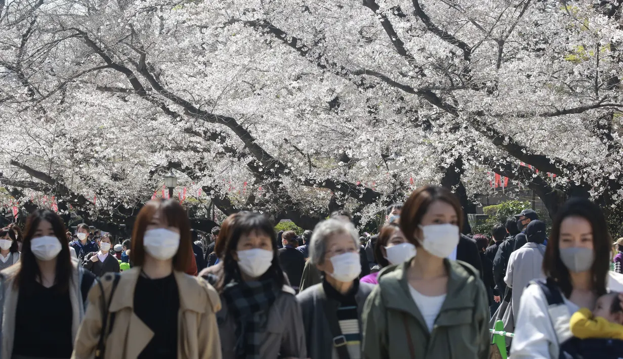 Orang-orang yang memakai masker berjalan di bawah bunga sakura di Tokyo, Selasa (23/3/2021). Mendekati musim semi dan mekarnya bunga sakura, banyak pemerintah daerah yang terus meminta warganya untuk tidak mengadakan pesta melihat bunga sakura (hanami). (AP Photo/Koji Sasahara)
