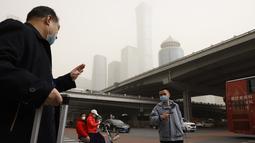 Warga yang mengenakan masker melintasi persimpangan saat badai pasir di Beijing (28/3/2021). Pada Senin (15/3/2021) pagi, langit Beijing menjadi jingga, membatasi jarak pandang hingga kurang dari 1.000 meter dan mengganggu lalu lintas. (AP Photo/Ng Han Guan)