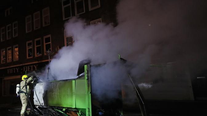 Seorang petugas pemadam kebakaran memadamkan kontainer yang dibakar selama protes menentang jam malam di Rotterdam, Belanda, Senin (25/1/2021). Kendaraan, toko-toko, dan pusat tes COVID-19 menjadi sasaran amuk massa. (AP Photo/Peter Dejong)