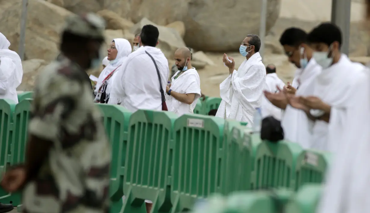 Polisi Saudi berjaga di depan jemaah Muslim yang sedang berdoa di Arafah selama ibadah haji di luar kota suci Mekah, Arab Saudi (19/7/2021). Sekitar 60 ribu jemaah haji mulai memadati kawasan Arafah, pada Senin pagi 9 Dzulhijjah 1442 Hijriah atau bertepatan pada 19 Juli 2021. (AP Photo/Amr Nabil)