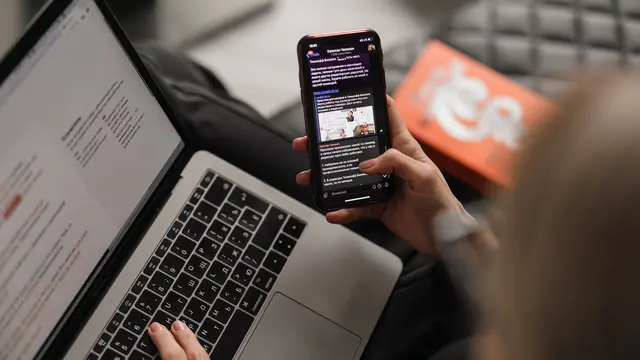 Young woman working at a laptop while browsing her phone
