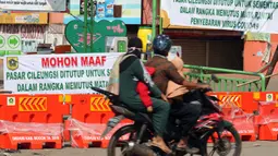 Warga melintasi pintu masuk kawasan Pasar Cileungsi yang dipenuhi spanduk penutupan, Kabupaten Bogor, Selasa (2/6/2020). Penutupan sementara kegiatan jual beli di Pasar Cileungsi terkait adanya tujuh pedagang yang positif terinfeksi virus COVID-19. (Liputan6.com/Helmi Fithriansyah)