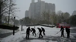 Pekerja menyekop salju di depan sebuah mal di Beijing, China, Minggu (7/11/2021). Badai salju awal musim telah menyelimuti sebagian besar Cina utara termasuk ibu kota Beijing, mendorong penutupan jalan dan pembatalan penerbangan. (Noel Celis / AFP)