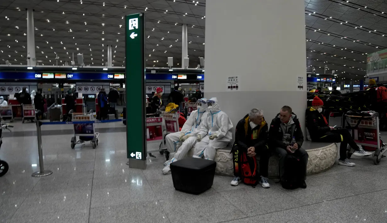 Pekerja Olimpiade dengan pakaian pelindung duduk di samping penumpang di bandara Internasional Ibu Kota Beijing setelah Olimpiade Musim Dingin 2022, di Beijing, China, Senin (21/2/2022). (AP Photo/Natacha Pisarenko)