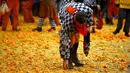 Seorang peserta mengumpulkan jeruk di tanah saat perang-perangan selama karnaval di kota Ivrea, Italia, Minggu (7/2). Peserta yang dibagi menjadi dua tim ini saling melempar jeruk menggunakan kostum dan aksesoris lengkap. (REUTERS/Stefano Rellandini)