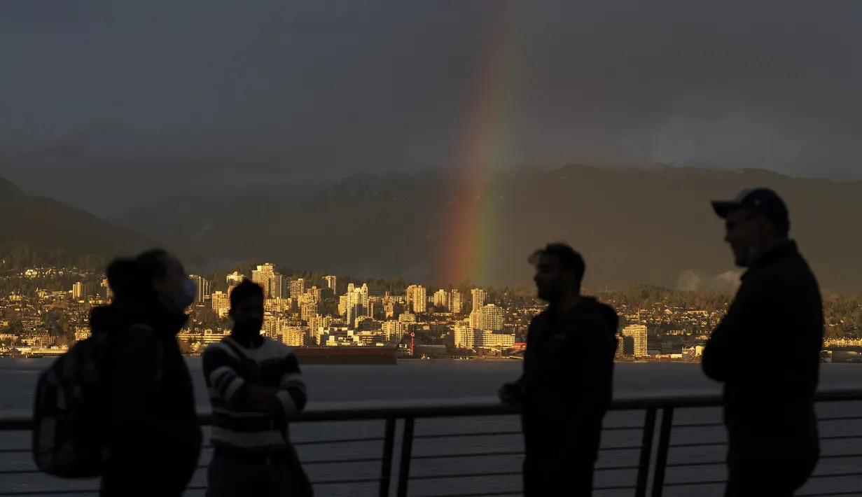 Siluet orang-orang  di depan pelangi di pusat kota Vancouver, British Columbia, Kamis (18/3/2021).  Lansekap kota ini didominasi Pegunugan Pesisir Utara dan pemandangan pada hari yang cerah. (Jonathan Hayward / The Canadian Press via AP)