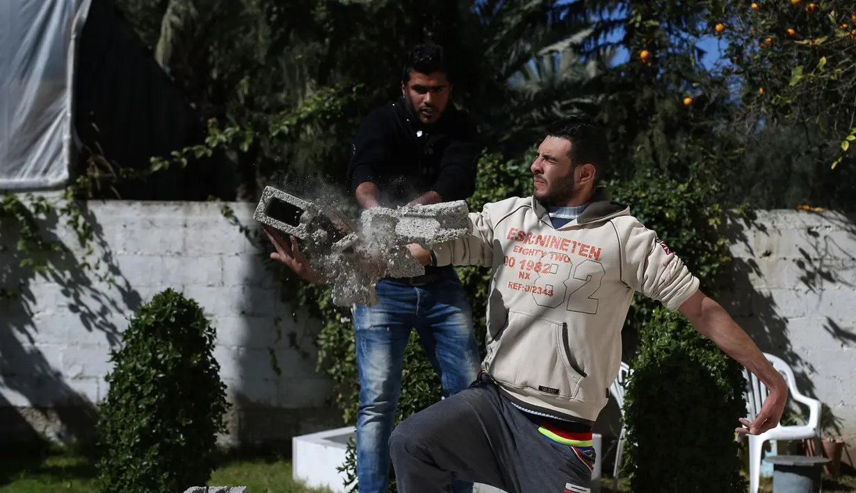 Aksi Mohamed Barka, pria yang dijuluki "Super Hero" asal Palestina yang menjadikan lengannya sebagai bantalan untuk menghancurkan batu bata beton di Deir Al-Balah, Gaza Tengah, Kamis (4/2). (MOHAMMED ABED/AFP)