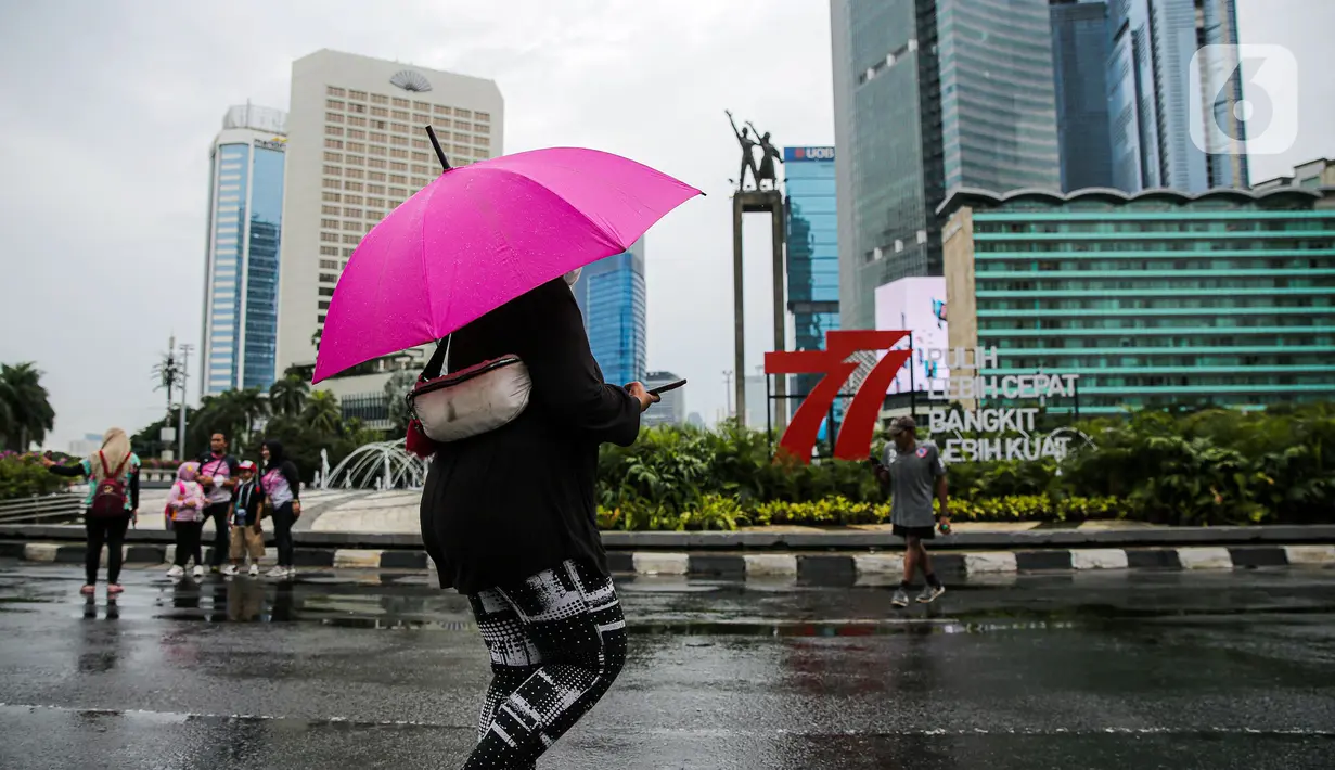 Warga berjalan sambil menggunakan payung saat Car Free Day (CFD) di kawasan Bundaran HI, Jakarta, Minggu (2/10/2022). Meski diguyur hujan deras sejak pagi, warga tetap antusias untuk tetap berolahraga saat CFD. (Liputan6.com/Faizal Fanani)