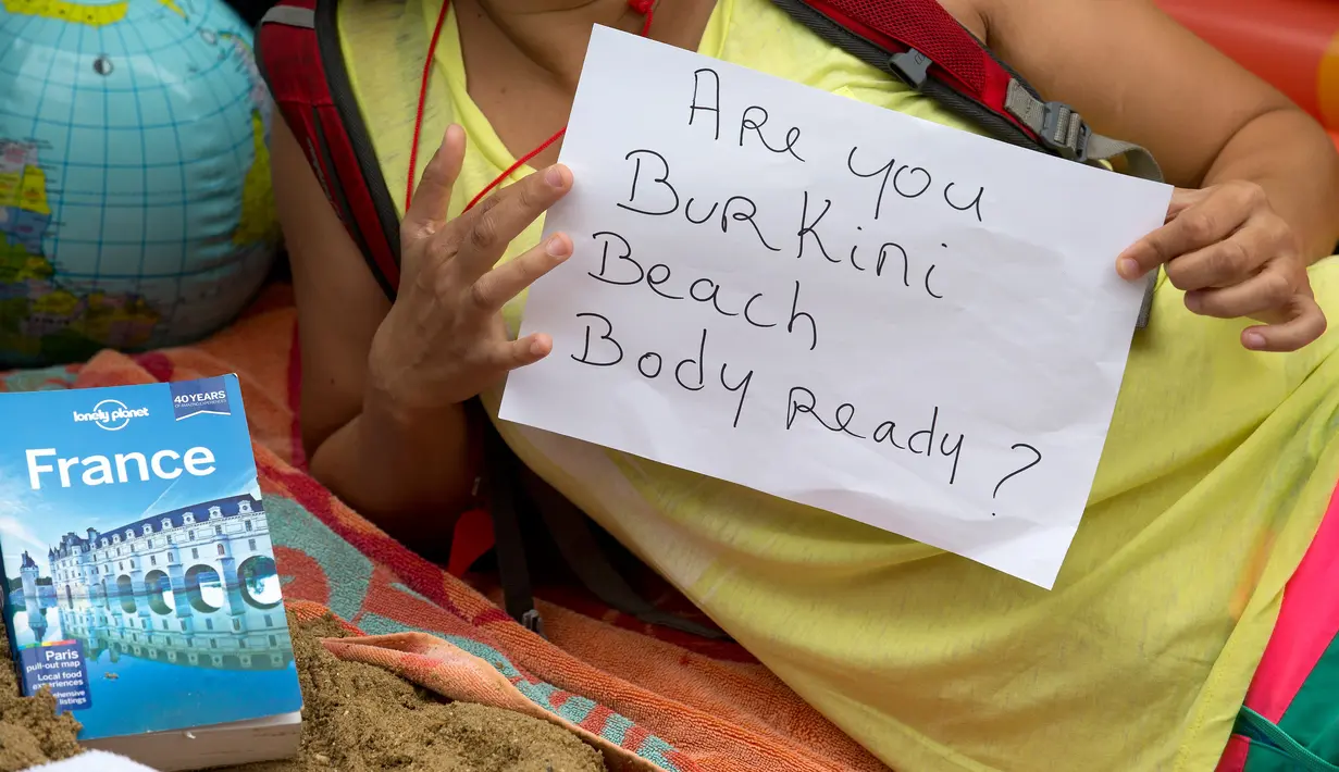 Seorang pengunjuk rasa memegang kertas berisi protes sambil bersantai di atas tumpukan pasir di luar kedutaan Prancis di London, Inggris, Kamis (25/8). Mereka memprotes larangan burkini di beberapa kota pesisir di Prancis. (AFP PHOTO/JUSTIN Tallis)
