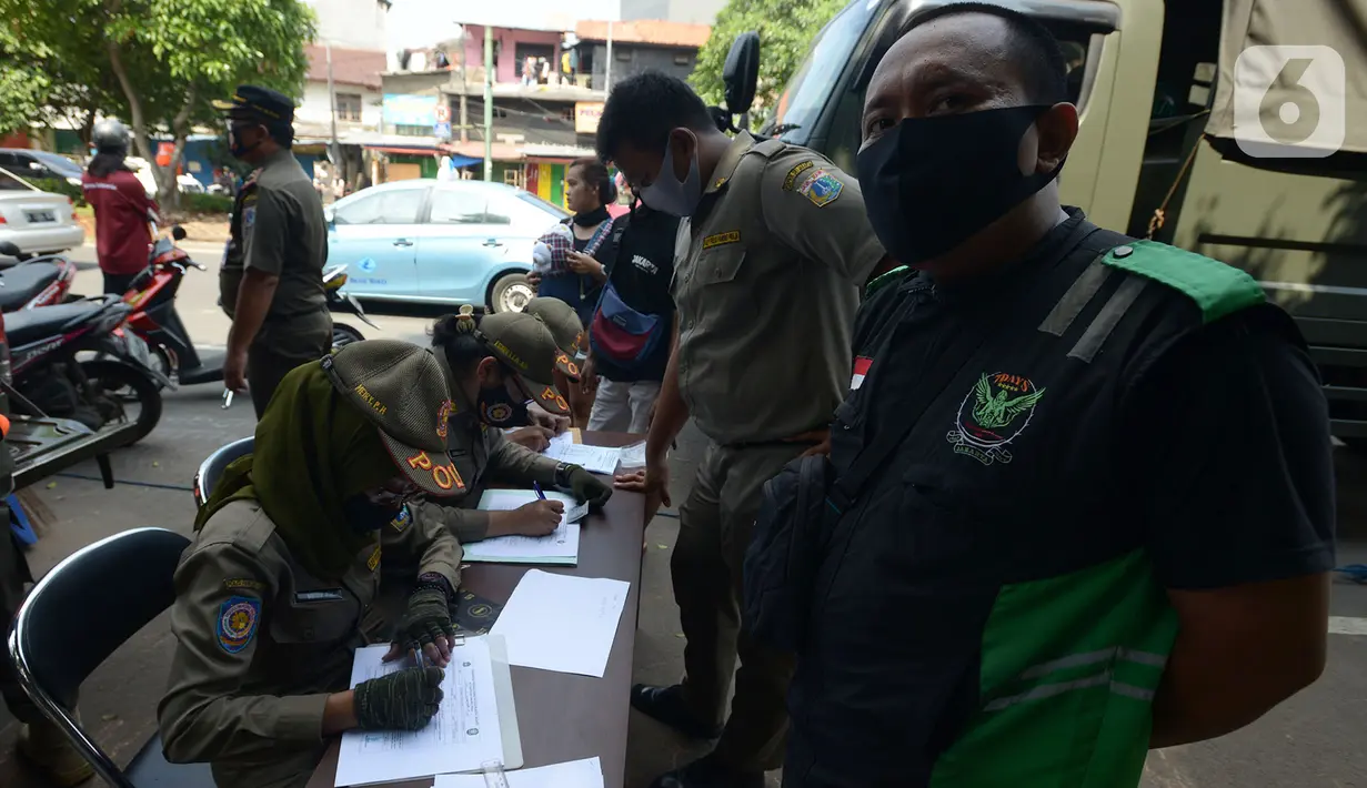 Petugas Satpol PP mendata warga yang terjaring razia pelanggar PSBB (Pembatasan Sosial Berskala Besar) di Pasar Gembrong, Jakarta, Selasa (2/6/2020). Para pelanggar aturan PSBB tersebut dijatuhi sanksi membayar denda atau melakukan pelayanan sosial. (merdeka.com/Imam Buhori)