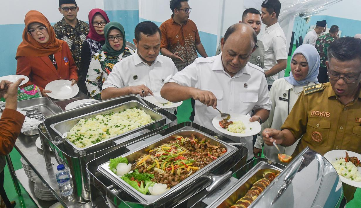 Dapur SPPG Terintegrasi di Tanah Sareal ditargetkan mampu melayani hingga 28.000  pemberi manfaat. Kehadiran program ini diharapkan menjadi contoh pengelolaan layanan gizi yang tidak hanya berfokus pada pemenuhan kebutuhan anak, tetapi juga berkontribusi nyata terhadap penguatan ekonomi masyarakat di sekitarnya. Tampak dalam foto, Kepala Badan Gizi Nasional (BGN), Dadan Hindayana mencoba makan bergizi gratis saat Grand Launching Nasional Satuan Pelayanan Pemenuhan Gizi (SPPG) Terintegrasi di Lapangan Dapur SPPG-MBG kawasan Tanah Sareal Kota Bogor, Jawa Barat, Selasa (23/12/2025). (merdeka.com/Arie Basuki)