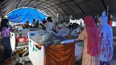 Orang-orang yang terluka dalam gempa dengan magnitudo 6,2 beristirahat di tempat penampungan sementara di luar Rumah Sakit Regional Sulbar, Mamuju, Sulawesi Barat, Minggu (17/1/2021). Mereka dirawat di dalam tenda darurat untuk mengantisipasi gempa susulan. (ADEK BERRY/AFP)