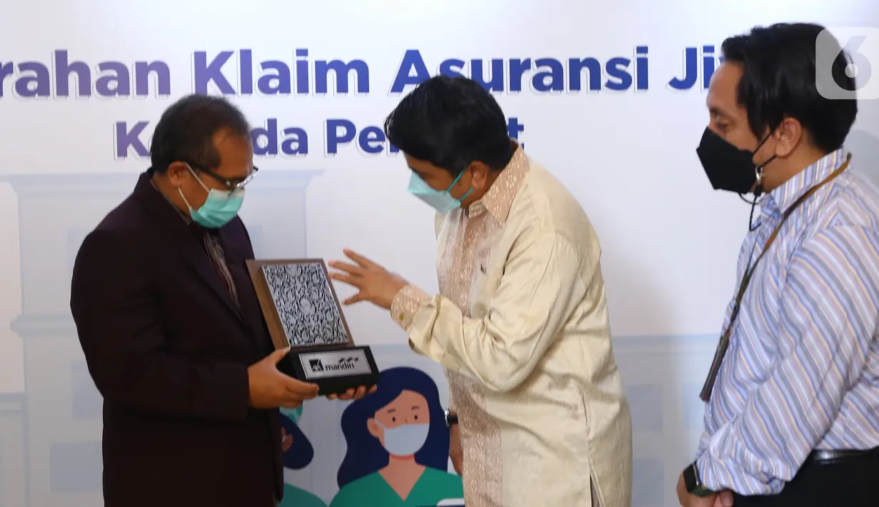 Direktur AXA Mandiri Uke Giri Utama (tengah) memberikan cinderamata kepada Ketua Umum DPP Persatuan Perawat Nasional Indonesia (PPNI) dr. Harif Fadillah (kiri) menyerahkan klaim tahap pertama kepada 170 tenaga kesehatan yang gugur menangani COVID-19 di Jakarta (26/8/2021). (Liputan6.com/HO/Alwi)