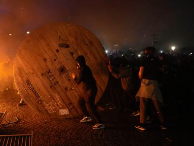 Demonstran menggulung gulungan kabel kayu ke barikade yang terbakar saat protes RUU Pensiun di Paris, Prancis, Jumat (17/3/2023). (AP Photo/Lewis Joly)