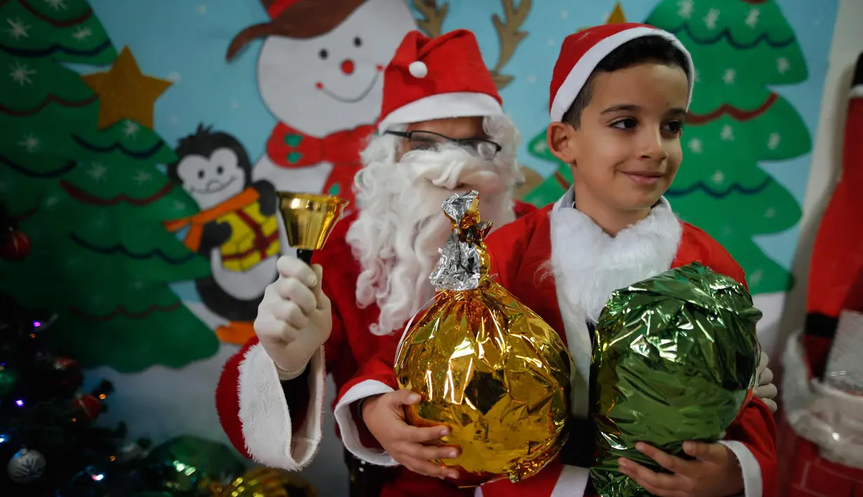Seorang anak laki-laki Palestina sambil membawa kado foto bersama dengan santa claus  saat perayaan menyambut Hari Natal di Sekolah Amerika di Kota Gaza (20/12).  (AFP Photo/Mohammed Abed)