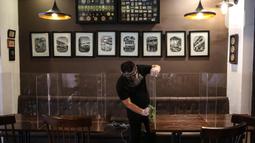 Pekerja membersihkan papan pelindung akrilik usai digunakan pengunjung di The Atjeh Connection Coffee and Resto, Jakarta, Senin (8/6/2020). Tempat ini siap menerapkan protokol kesehatan dalam menerapkan tatanan kehidupan baru atau ‘new normal’. (Liputan6.com/Faizal Fanani)