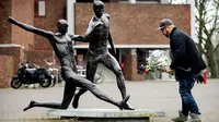 Seorang pria akan meletakan bunga di depan patung Johan Cruyff yang terdapat di sekitar Stadion Amsterdam Arena, Amsterdam, Kamis (24/3/2016). Mantan bintang timnas Belanda itu meninggal pada usia 68 tahun. (AFP/Koen Van Weel)