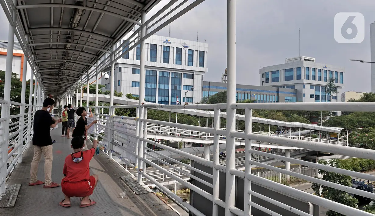 Anak-anak bermain layang-layang di Jembatan Penyeberangan Orang (JPO) kawasan Jakarta, Kamis (11/6/2020). Minimnya ruang terbuka di sekitar tempat tinggal anak-anak itu menyebabkan mereka terpaksa bermain layang-layang di JPO yang sangat berisiko dan berbahaya. (merdeka.com/Iqbal Nugroho)