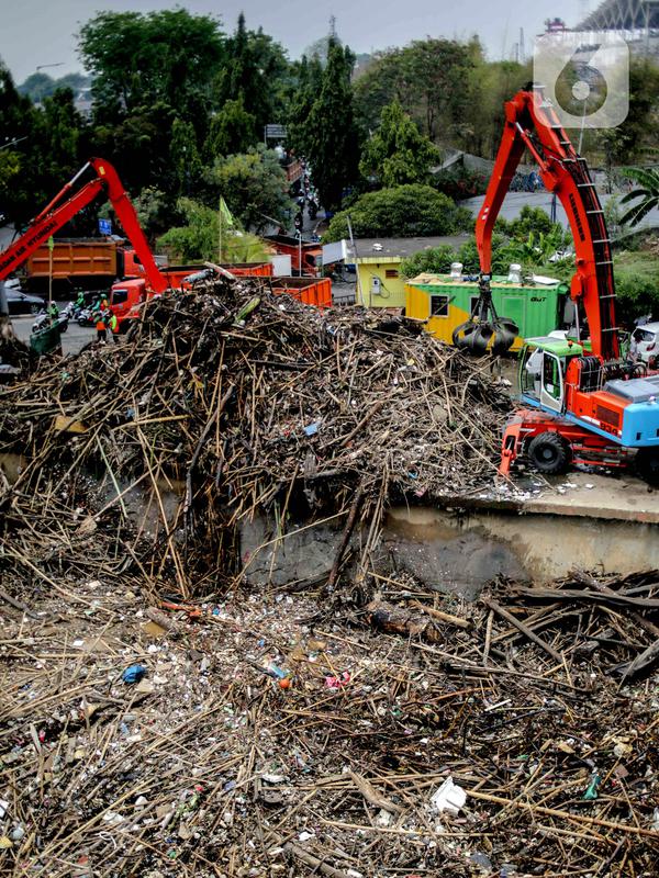 Petugas dibantu alat berat membersihkan sampah kayu dan bambu yang tersangkut di Pintu Air Manggarai, Jakarta, Rabu (9/10/2019). Sampah tersebut merupakan kiriman dari Bogor usai diguyur hujan deras tadi malam. (Liputan6.com/Faizal Fanani)