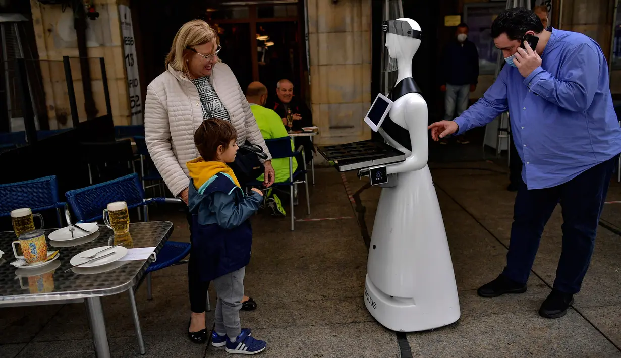 Santo Munoz (kanan) menyiapkan robot yang dikenal sebagai "Alexia" untuk melayani pengunjung sebuah bar di alun-alun Plaza del Castillo, di Pamplona, Spanyol pada 5 Juni 2020. Robot tersebut digunakan untuk mengurangi penyebaran virus corona Covid-19. (AP Photo/Alvaro Barrientos)
