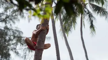 Seorang pria memanjat pohon saat mengikuti kejuaraan dunia pertama panjat pohon kelapa di Papeete, Polinesia (15/7). Kompetisi ini juga sebagai bagian dari festival budaya besar bagi orang Polinesia. (AFP Photo/Gregory Boissy)