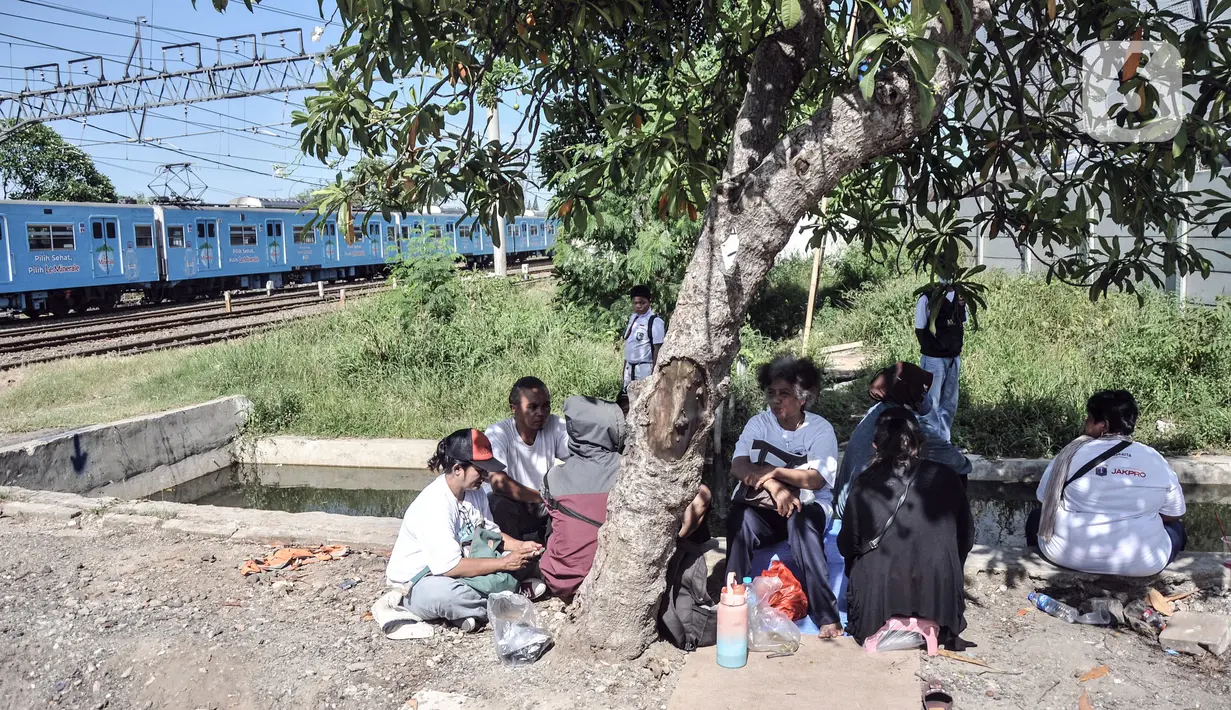 Warga berteduh di bawah pohon saat berunjuk rasa di depan gerbang Kampung Susun Bayam, Jakarta Utara, Senin (21/11/2022). Berdasarkan kesepakatan, seharusnya warga sudah mulai bisa menempati hunian pada 20 November 2022 kemarin. (merdeka.com/Iqbal S. Nugroho)