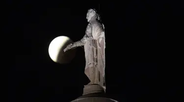 Bayangan bumi menutupi bulan purnama selama gerhana bulan sebagian atau parsial terlihat di dekat patung George Washington di atas Monumen Washington Baltimore, di Baltimore, Jumat (19/11/2021).. (AP Photo/Charlie Riedel)