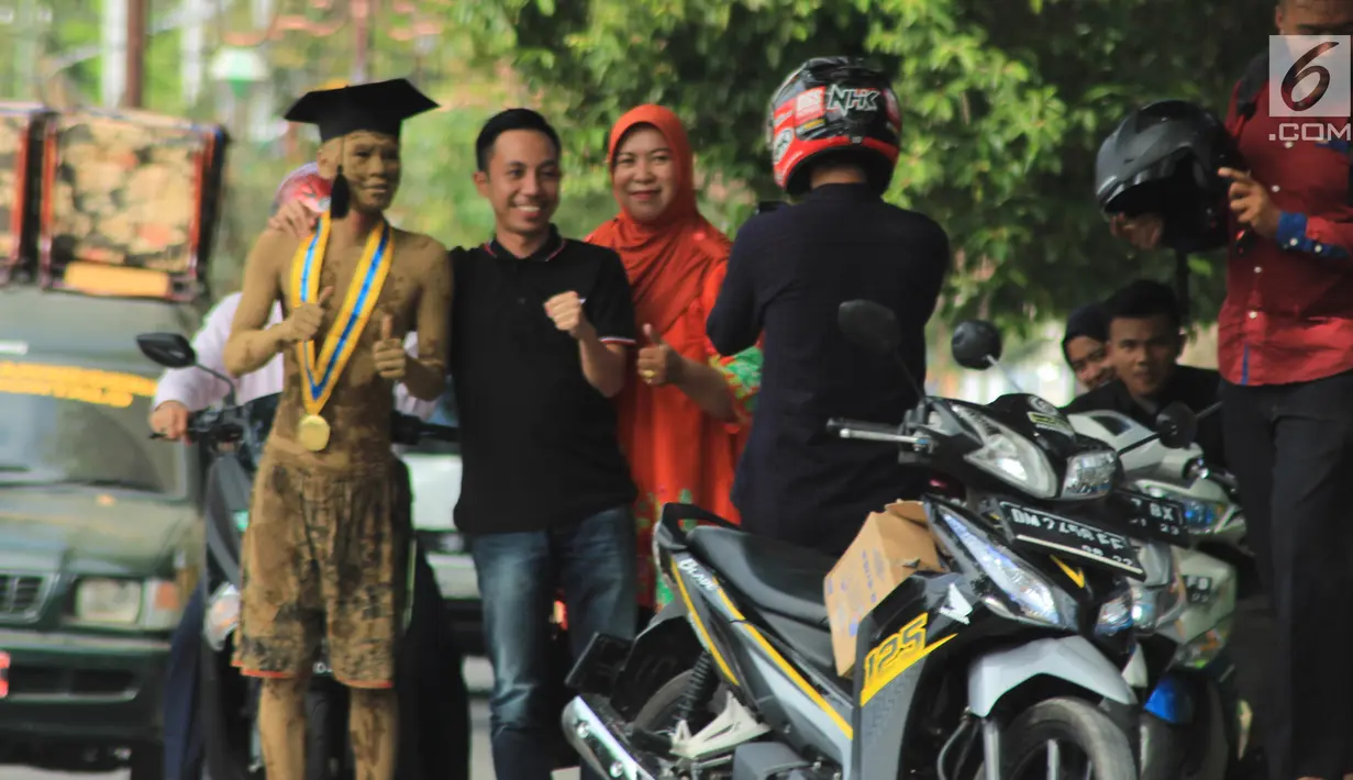 Warga berfoto bersama mahasiswa UniversItas Gorontalo, Indra Nodu yang melakukan aksi jalan kaki dari kampus ke rumahnya di Desa Posso, 4 Agustus 2018. Tubuhnya berlumur lumpur basah, Indra berjalan di tengah terik matahari. (Liputan6.com/Arfandi Ibrahim)